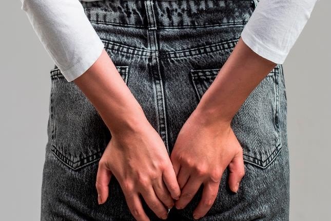 Pessoa de costas, em jeans, segurando a região das nádegas, indicando dor ou desconforto anal