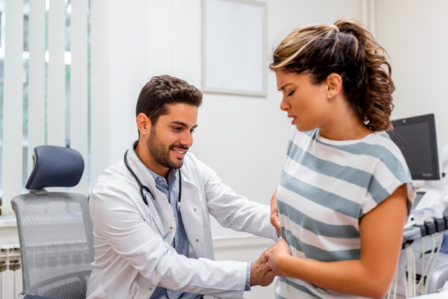 Medico examinando paciente com mao no quadril indicando dor